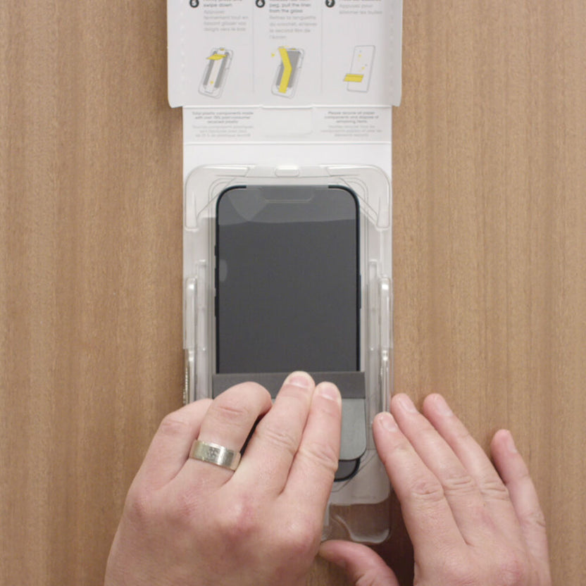 Person applying a screen protector to a smartphone on a wooden surface