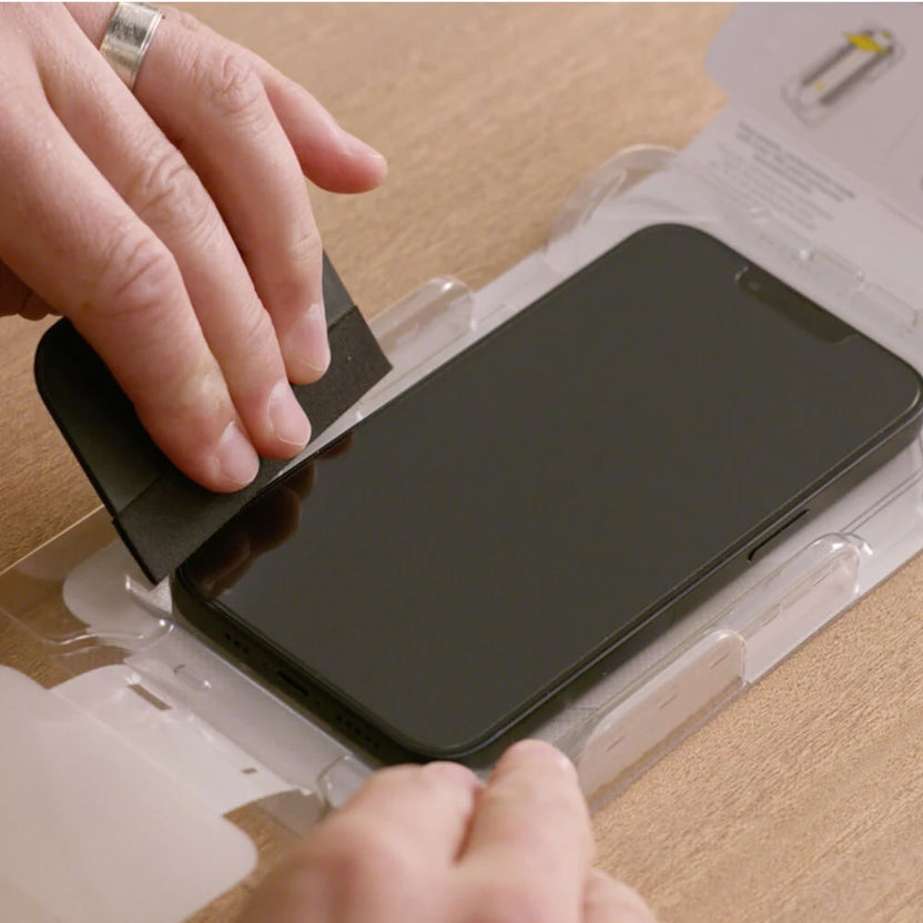 Person applying a screen protector to a smartphone on a wooden surface