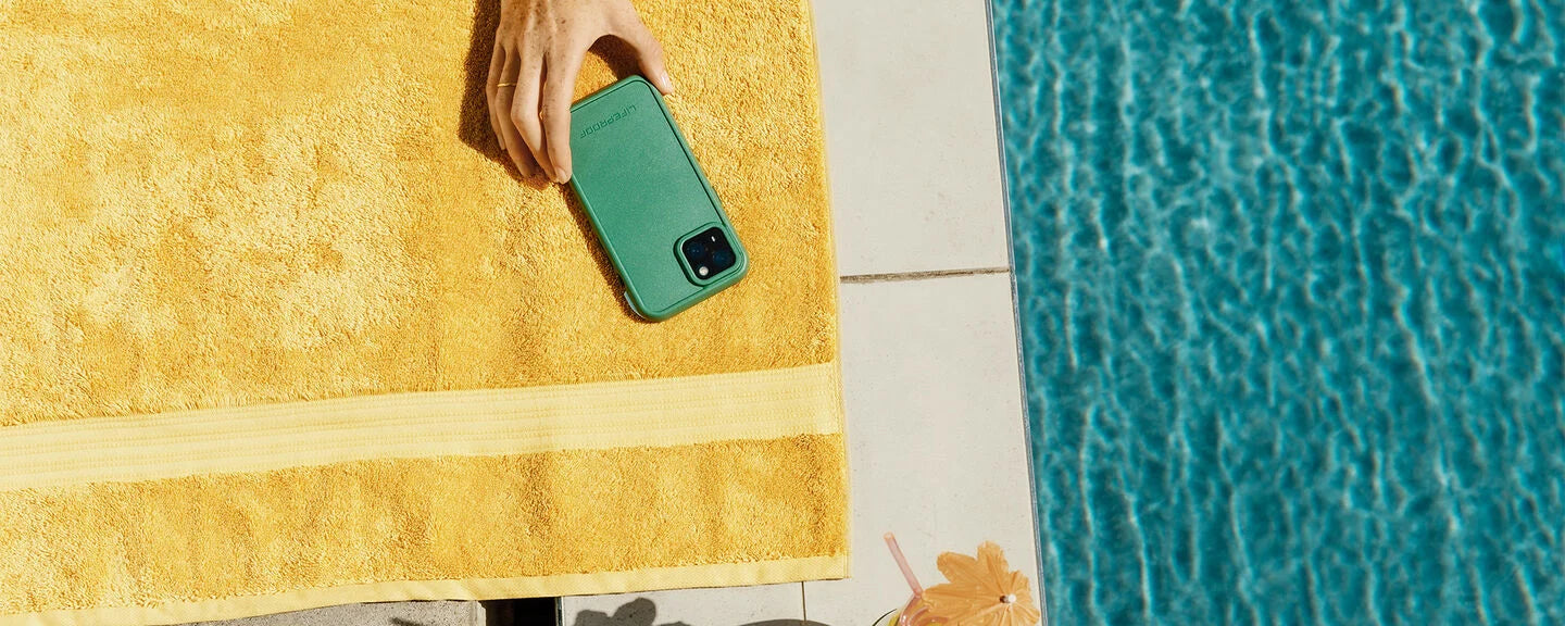 Person holding a green phone on a yellow towel by a pool