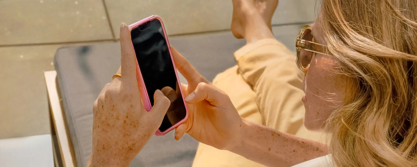 Person holding a smartphone with a pink case, sitting outdoors.