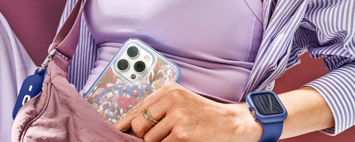 Person holding a phone case with floral design and wearing a smartwatch, sitting on a pink chair.